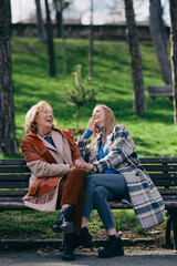 A grandmother is laughing and having fun with her adolescent granddaughter while sitting on the park bench. - 506834845