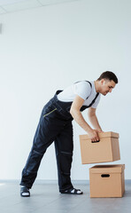 A caucasian man is stacking two heavy cardboxes for a relocation. A worker in uniform. Fresh renovation, white walls.