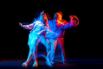 Dynamic portrait of stylish man and girl dancing hip-hop in sportive style clothes on dark background at dance hall in mixed neon light. Youth culture, breakdance, movement