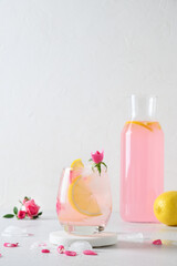 Pink alcoholic rose beverage or lemonade, cocktail with rose flowers on white background. Close up....