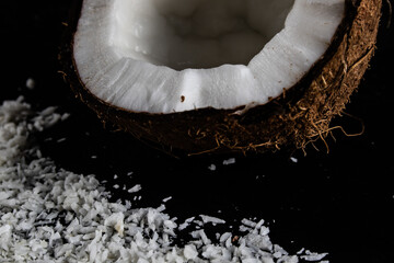 Cutaway coconut on the black background. View from above. Coconut and coconut flakes on a black glass table.