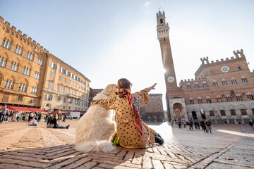 Woman sitting with her dog on main square of Siena city with a town hall on background. View from...