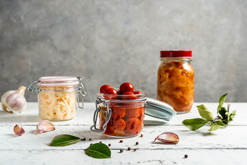 Pickled tomatoes, kimchi, cabbage in jar with garlic, oil, pepper and bay leaves on white wooden...