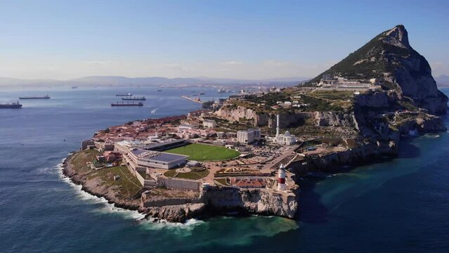 Rugby stadium and white mosque at Europa point with the lighthouse above the cliffs and in the background ships anchored in Bay of Algeciras and the upper rock of Gibraltar. Wide drone trucking shot