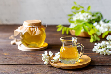 Acacia honey in glass jar with flowers aside on wooden background