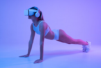 Athletic young female in sportswear and vr headset standing in plank position in neon light