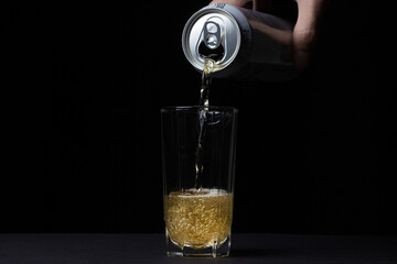 Glass of beer on a black background. Beer is poured into a glass from an aluminum can. Alcoholic...