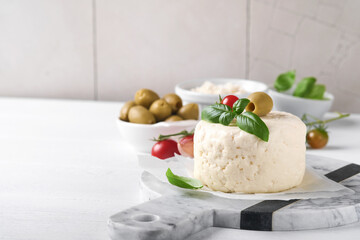 Ricotta cheese. Homemade Ricotta cheese with basil, garlic, tomatoes and green olives on parchment paperback and stand on old beige tiles background. Italian food.  Selective focus.