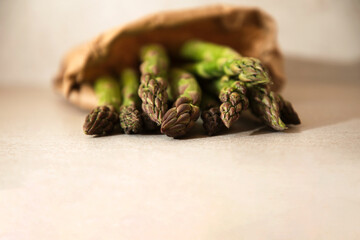 Ripe fresh asparagus in a paper bag on a beige table close-up, selective focus