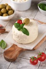 Ricotta cheese. Homemade Ricotta cheese with basil, garlic, tomatoes and green olives on parchment paperback and stand on old beige tiles background. Italian food.  Selective focus.