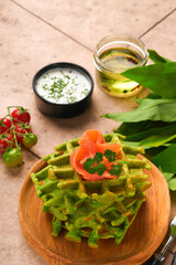 Green Belgian waffles. Spinach or wild garlic or pesto waffles with red salmon and cream sauce on old beige tile table background. Delicious breakfast, snack, brunch on  old beige tiles background.