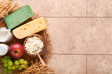 Happy Shavuot. Background for Shavuot celebration. Milk and cheese, ripe wheat and fruits, blue wooden background. Dairy products over old cracked tile wall. Shavuot concept. Top view. Mock up.