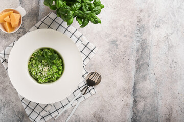 Italian risotto. Delicious risotto in white plate with pesto sauce or wild garlic pesto, basil, parmesan cheese and glass of white wine on old light grey table background. Top view with copy space.