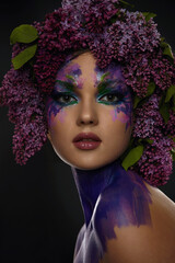Portrait of a beautiful young girl with exquisite fantasy make-up and lilac branches in her hair