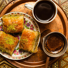 Still life with hot oriental coffee brewed in cezve. On the Arabic table is a small coffee cup and delicious honey baklava with pistachios on a saucer. View from above