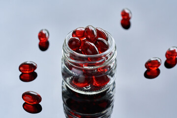 Krill oil pills or softgels in a glass jar on a glossy background