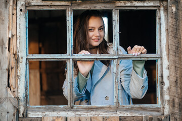 girl looks out the window from an old wooden house