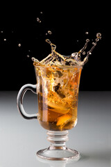 Cold tea splash on the transparent tea cup, with lemon, dark background