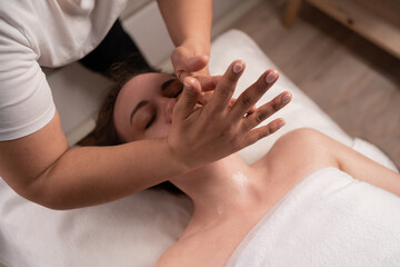 Obraz na płótnie Canvas Beauty treatment concept, woman having massage of face in spa salon, masseur doing facial massage on woman face, spa skin and body care.