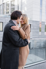 young romantic couple in trendy coats embracing on city street.