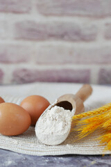 wheat flour in a wooden spoon and eggs on table 