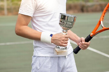 Horizontal view of young unrecognizable amateur tennis player holding an award winning cup on a...