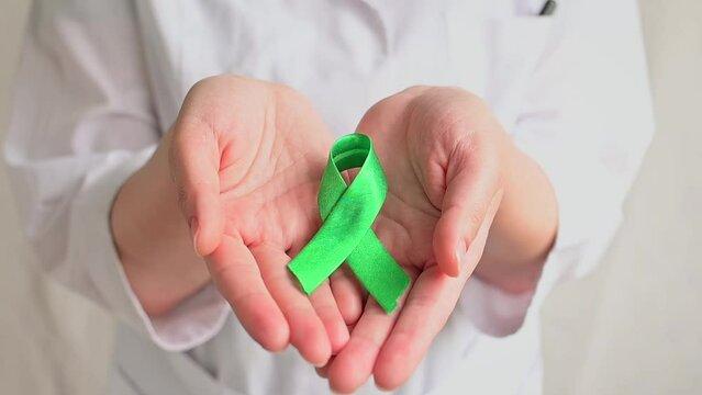 World bipolar day. Doctor in white coat holds green ribbon. Mental health awareness day, Depression, Cerebral palsy. World kidney day.