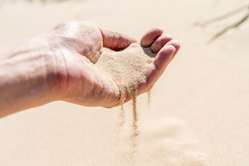 Sand spilling out pouring flow of the hand in the sandy desert dunes on bright sunny day. Transience of time. Selective focus.