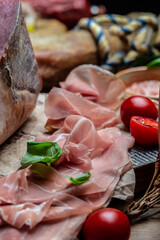 prosciutto on wooden board with fresh basil and cherry tomatoes, vertical image. top view. place for text