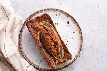 Chocolate banana bread with walnuts on a white plate with brown rim on a grey neutral background , top view