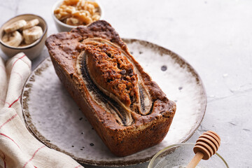 Chocolate banana bread with walnuts on a white plate with brown rim and ingredients on a grey neutral background