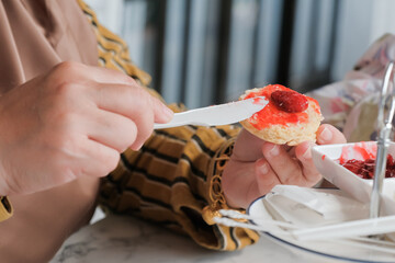 Close up view of a woman holding scone ready to put strawberry jam on scone
