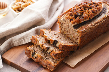 Chocolate banana bread with walnuts on a wooden board and ingredients on a grey neutral background