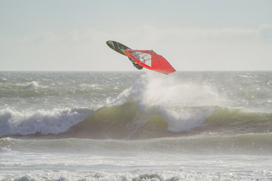 Windsurfer and wave in focus jumping over a big wave in Cape Town. Big wave splashing water windsurfing during sunset. Big Bay beach is an amazing place for sunset surf and windsurfing waves.
