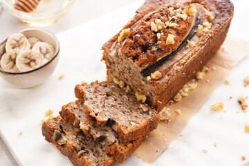 Chocolate banana bread with walnuts on a marble board and ingredients on a grey neutral background