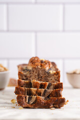 Slices of Chocolate banana bread with walnuts on a marble board and ingredients on a grey neutral background