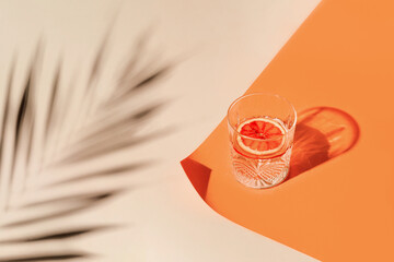 Glass of water with sliced blood orange on geometric background with shade. Summer refreshment concept. Sunlit flat lay. Minimal style.