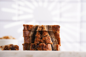 Slices of Chocolate banana bread with walnuts on a marble board and ingredients on a grey neutral background
