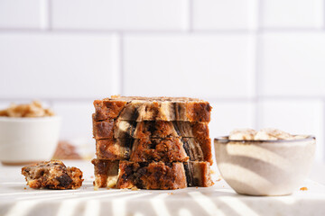 Slices of Chocolate banana bread with walnuts on a marble board and ingredients on a grey neutral background with creative lighting