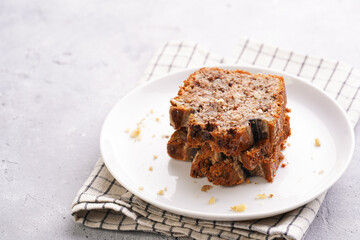 Slices of Chocolate banana bread with walnuts on a checkered kitchen napkin and ingredients on a grey neutral background
