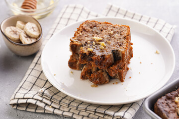 Slices of Chocolate banana bread with walnuts on a checkered kitchen napkin and ingredients on a grey neutral background