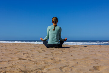 Fototapeta premium woman sitting on the beach facing east with arms open meditating