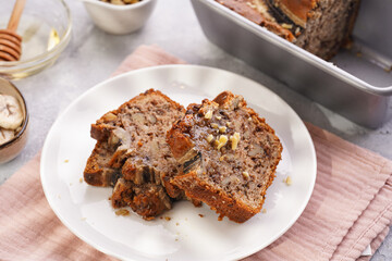 Slices of Chocolate banana bread with walnuts on a pink kitchen napkin and ingredients on a grey neutral background with creative lighting