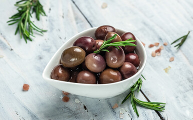 pink olives with fresh rosemary in a small bowl, on light wooden background. Long banner format. top view