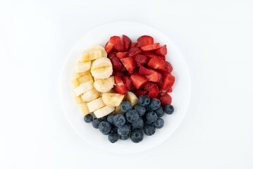 Pieces of strawberry, banana, blueberry on a white plate on a white background.