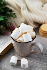 Blurred image of a cup of cocoa with marshmallows, cookies, a plaid and a book on a wooden background.