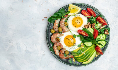 Ketogenic diet breakfast shrimps, prawns, soft fried egg, fresh salad, tomatoes, cucumbers and avocado on a light background. Keto, paleo lunch. Top view