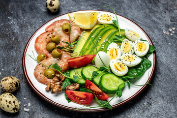Ketogenic breakfast. Keto low carb shrimps, prawns, quail eggs, fresh salad, tomatoes, cucumbers and avocado on a dark background. keto diet. Top view