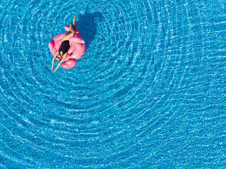 Aerial drone view of woman tourist enjoying travel holidays in swimming pool with flamingo float,...