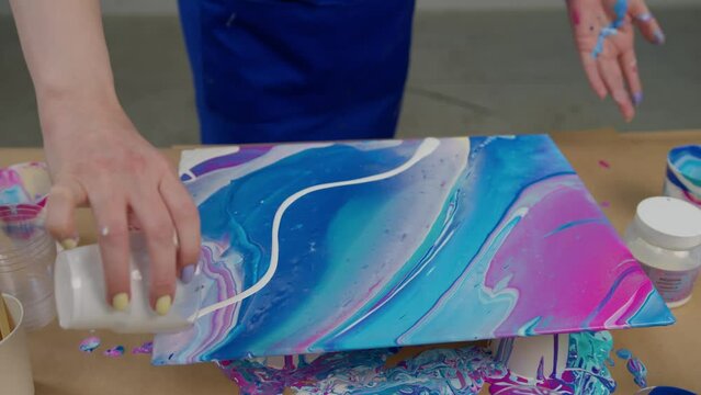 Women's hands hold a sheet of paper with multi-colored paint poured on it. Paint drips off a sheet of paper. Spilled paint. Drawing concept.